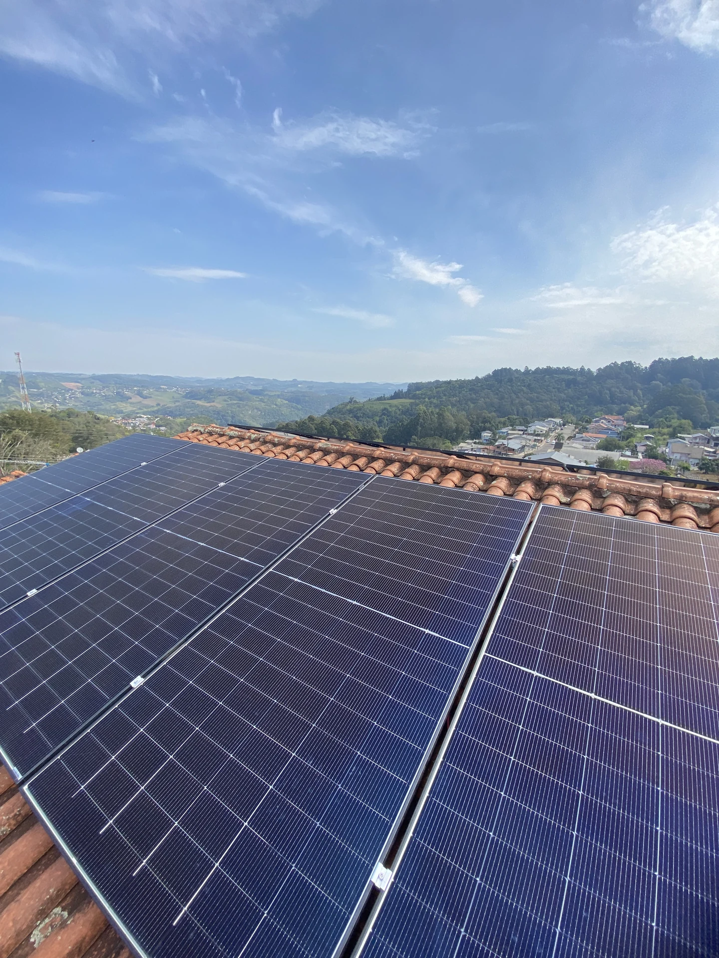 Módulos solares em telhado cerâmico, com a paisagem de morros ao fundo